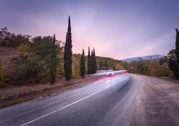 Mountain road with blurred cars in motion at sunset