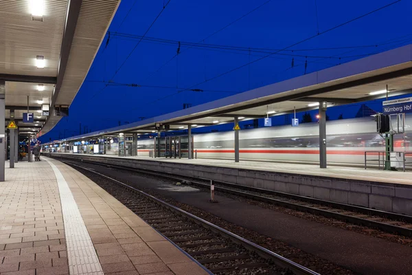 Modern railway station with high speed passenger train on railroad track in motion. Railway platform at night  in Nuremberg, Germany. Fast train..