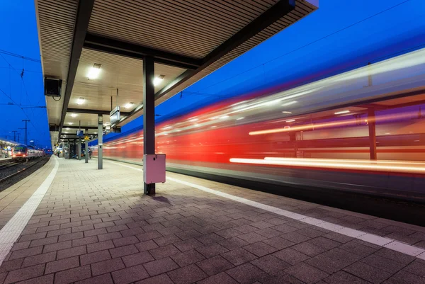 Modern railway station with high speed passenger train on railroad track in motion at night  in Nuremberg, Germany. Fast red commuter train.. Industrial landscape.