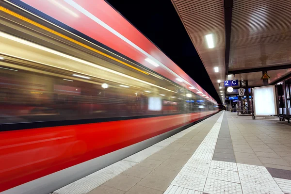Modern railway station with high speed passenger train on railroad track in motion at night  in Nuremberg, Germany. Fast blurred red commuter train.. Colorful industrial landscape.