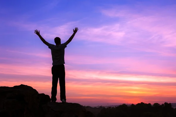 Silhouette of a man with raised-up arms at the sunset