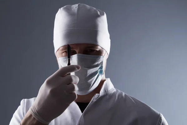 Male doctor in cap, mask and rubber medical gloves holding scalp