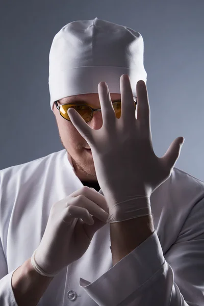 Male doctor in cap and glasses wear rubber medical gloves in con