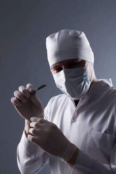 Male doctor in cap, mask and rubber medical gloves holding scalp