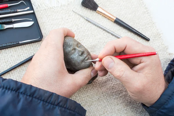 Hands of sculptor making sculpture head using tools