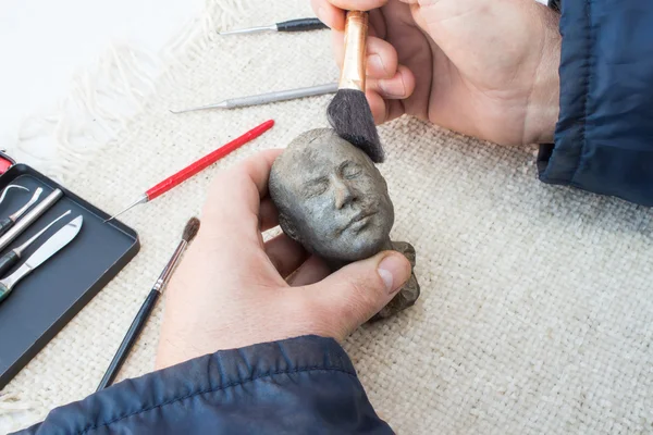 Hands of sculptor hold sculpture and clean it with brush