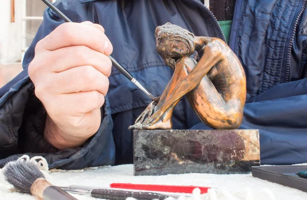 Hands of sculptor hold copper sculpture and clean it with brush