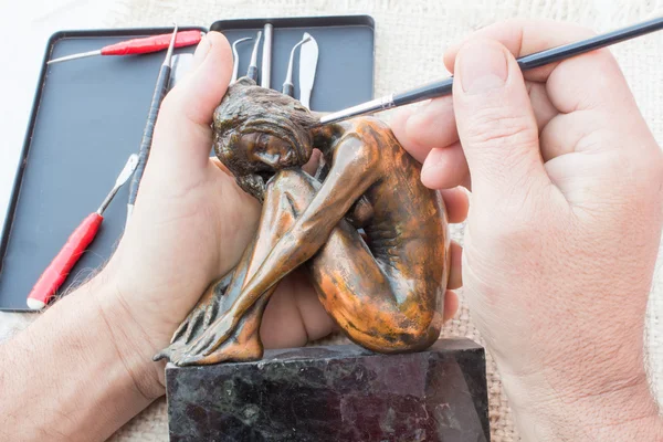 Hands of sculptor hold copper sculpture and clean it with brush