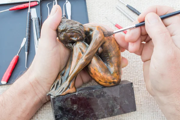 Hands of sculptor hold copper sculpture and clean it with brush