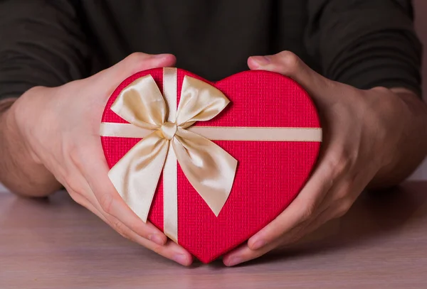 Two male hands holding red gift box in shape of heart