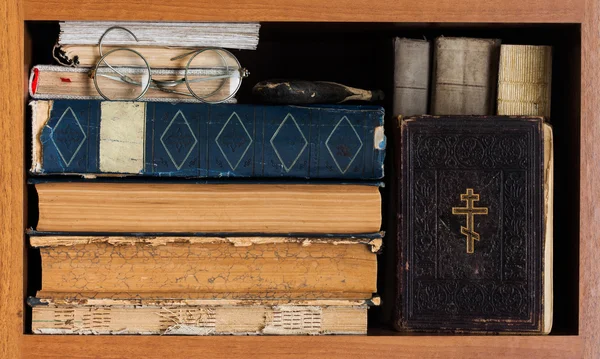 Library book shelf with Holy Bible book, aged books covers, spectacles. Vintage wooden frame. Christianity concept image.