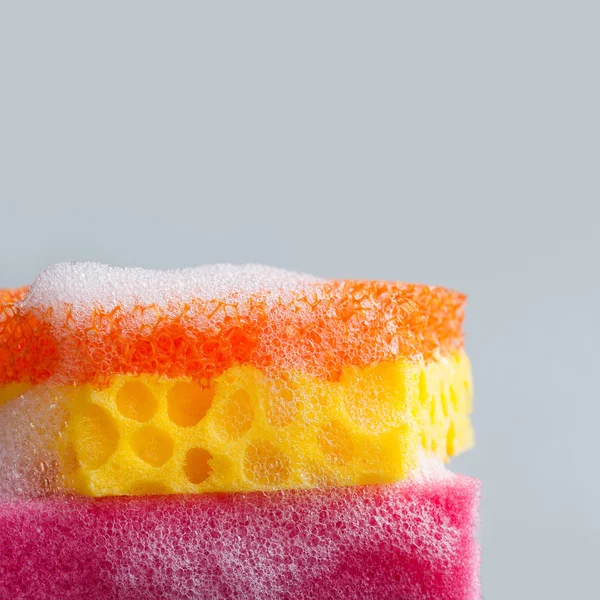 Colorful sponges with soap suds foam on gray background. Cleaning supplies concept. copy space, macro view