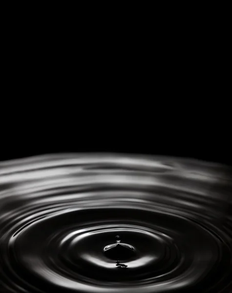 Dropping water bubble. Rings waves on black splashing background. Liquid splash, soft focus copy space.