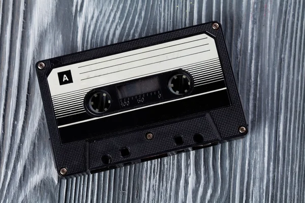 Music concept. Black audio cassette on the gray wooden background. Vintage, retro style. Soft focus.