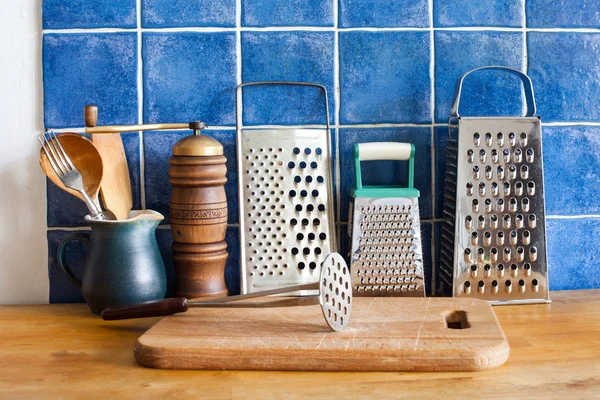 Kitchen still life. Vintage utensils. kitchenware graters, ceramic jug, spoons. cutting board. Blue tiles wall. wooden table background