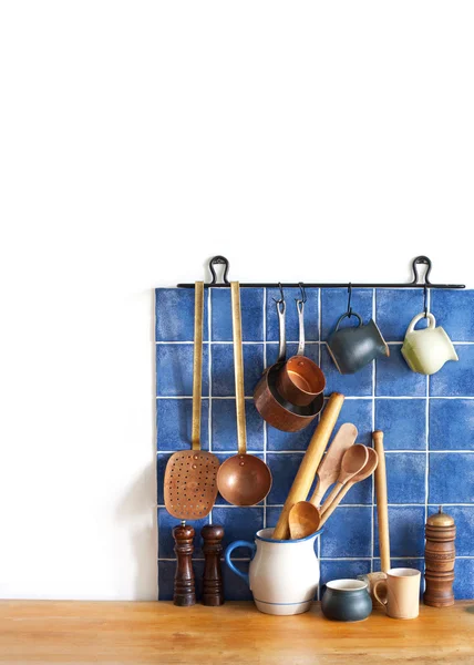 Kitchen brass utensils, chef accessories. Hanging copper kitchenware set. Blue tiles ceramic wall. spoon, pitchers, spices on the wooden table. White background. copy space.