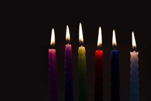 Colored candles on black background. six pieces. each candle silhouette with real flame. Light and darkness concept. Soft focus, copy space
