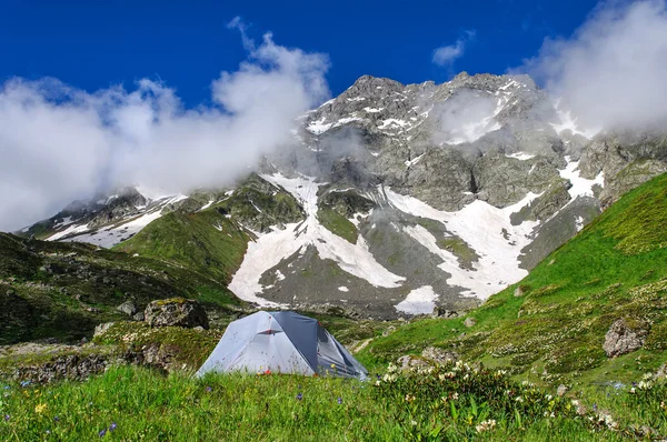 Gray tent in grass on background of mountains and rocks