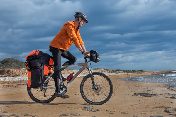 Man goes  sandy beach on mountain bike with big backpack.