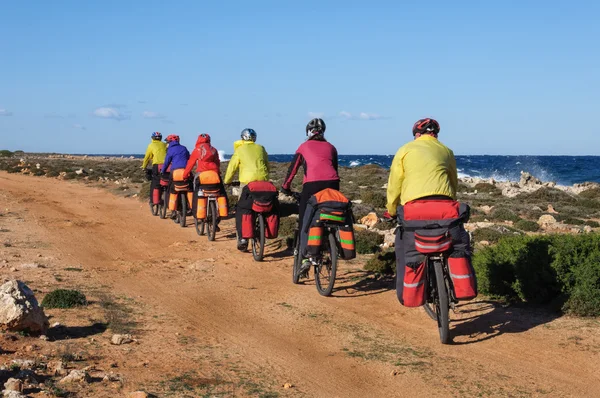 Group of cyclists riding sandy beach mountain bike with backpack.