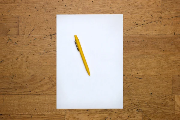 Pen on a blank paper sheet on a wooden table