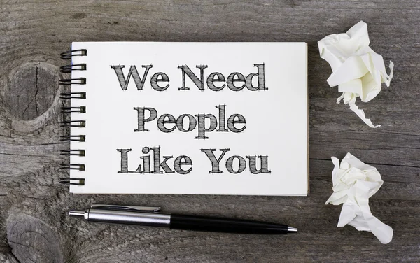 We Need People Like You. Text on a note pad on a wooden table.