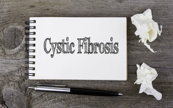 Cystic Fibrosis. Text on a note pad on a wooden table.