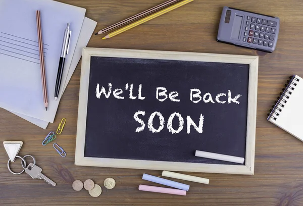 We\'ll Be Back Soon. Chalkboard on wooden office desk