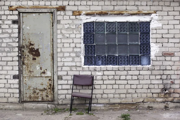 Brick wall with glass bricks window, rusted doors, old chair