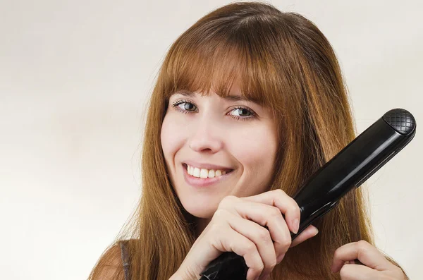 The woman straightens hair the curling iron