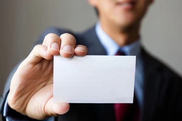 Young man in business suit holding white blank business card.