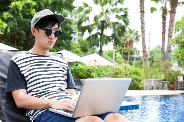 Asian man using a laptop in the pool on vacation - work anywhere and internet work concept