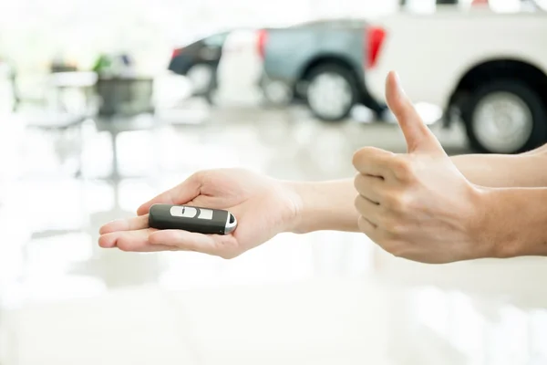 Human hands giving thumbs up with car key in car shoowroom