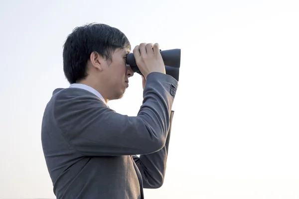 Asian businessman using binoculars during sunset being isolated from the sky - business vision / business opportunities / market watch concept.