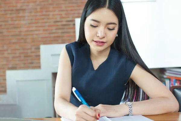 Beautiful Asian woman writing a notebook on table in modern interior