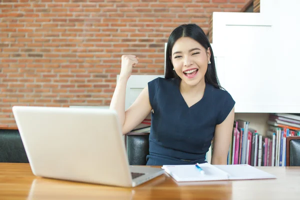 Excited Asian woman raising her arms while working on her laptop