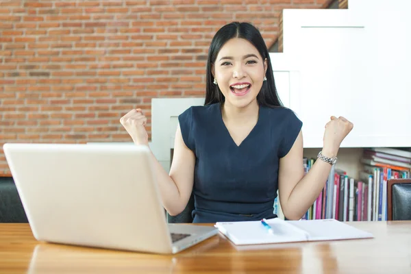 Excited Asian woman raising her arms while working on her laptop