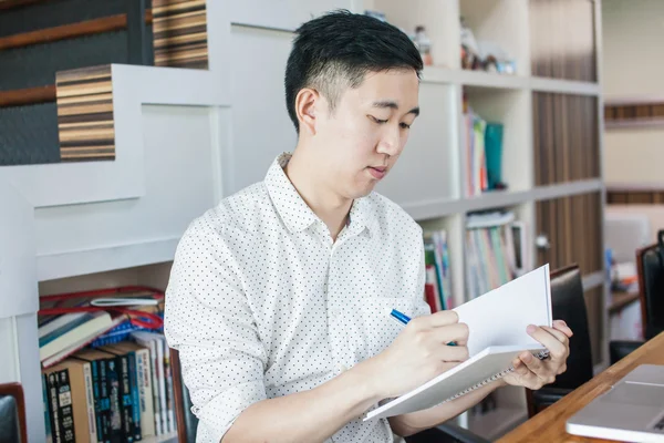 Young casual Asian man sitting and writing on notebook