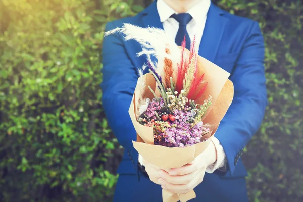 Young man in fashionable suit holding hipster hand-made bouquet