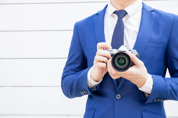 Stylish man in blue suit holding vintage camera in white vintage fence background.