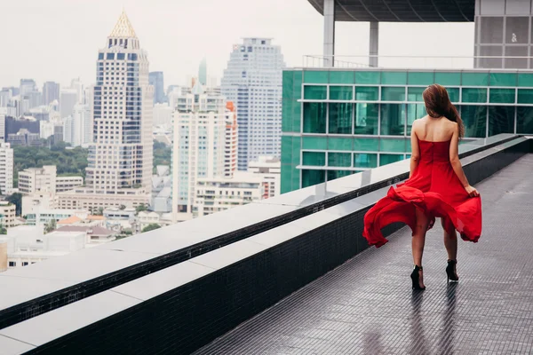 Woman in red walking on rooftop of building with cityscape scene