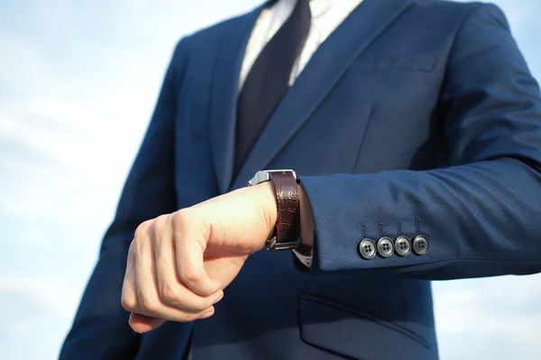 Fashionable businessman in elegant blue suit looking at luxury watch and waiting.