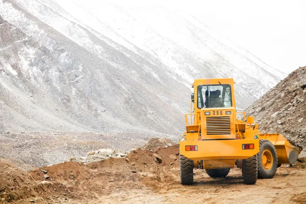 Big heavy machinery vehicle ploughing sand and stones to move path in snow mountain