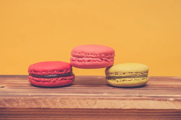 Pile of colorful macarons stacked up in yellow pastel isolated background on wood table