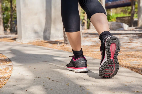 Running feet of young woman going by concrete trail in the park