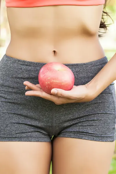 Healthy female holding apple at waist level outdoor in park