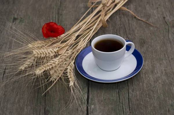 Cup of black coffee, bunch of wheaten ears and flower of poppy