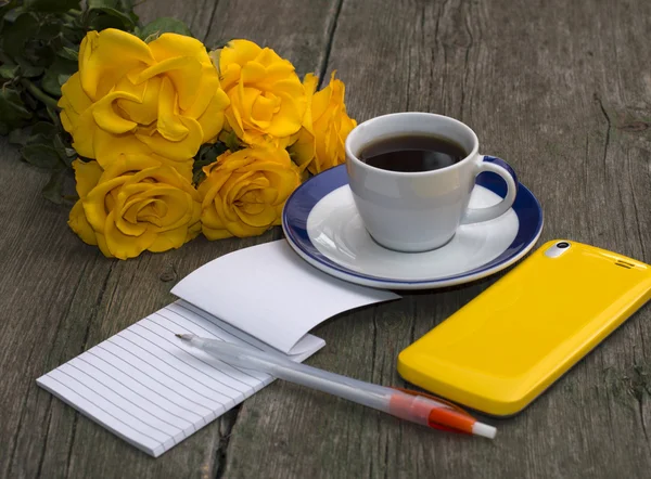 Bouquet of yellow roses, phone, notebook and coffee