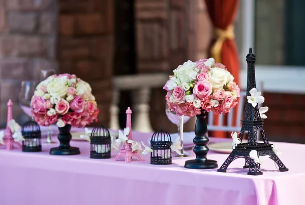 Wedding decoration of rose bouquets and small eiffel tower copies and symbolic birdcages on a wedding table with pink tablecloth during outdoor wedding ceremony