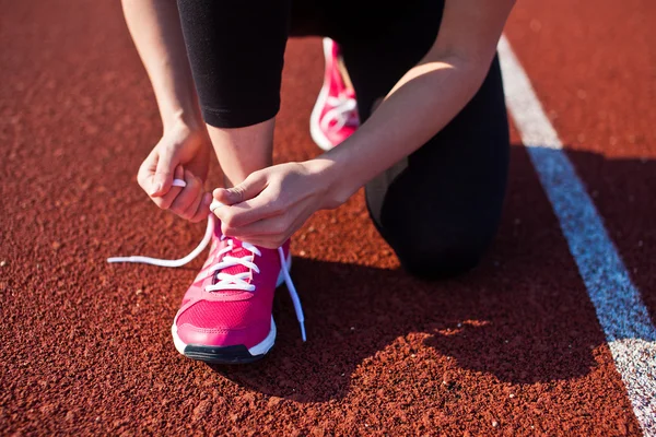 Young woman tying laces on her sports shoes before run on a running track at sunset. Focus on hands tying laces